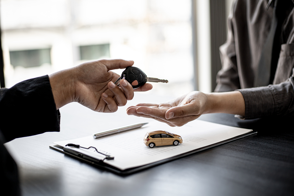Two people exchanging car keys over a table.