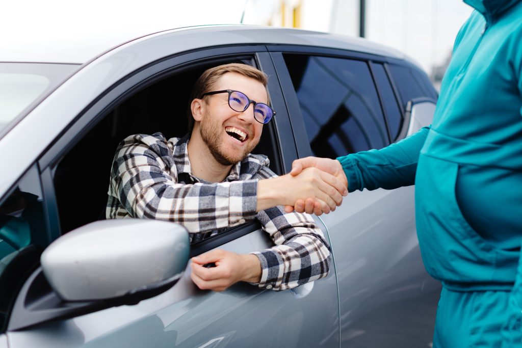 A person shaking hands from a car window.